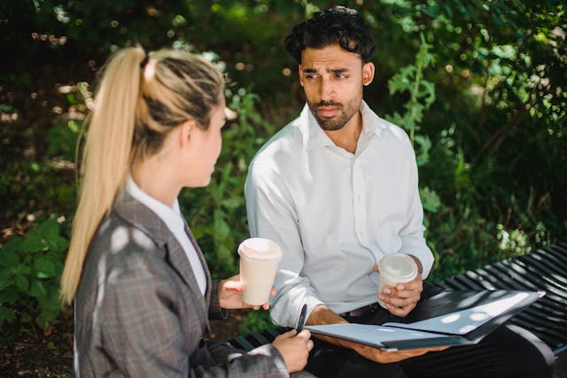 Two people sitting next to eachother outdoors while holding cups